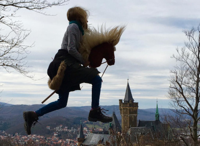 Sprung mit Steckenpferd vor Dorfhintergrund